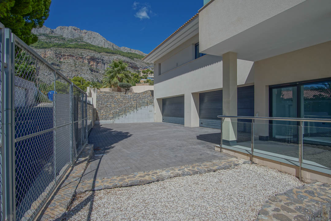 Haupteingang mit geräumiger Garage für mehrere Fahrzeuge, Natursteinmauern und gepflasterter Einfahrt vor der Kulisse der Sierra de Altea.
