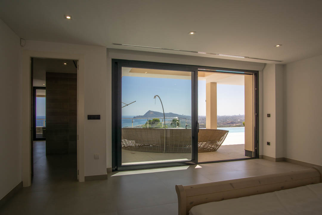 Schlafzimmer mit direktem Terrassenzugang durch bodentiefe Schiebetüren und Panoramablick auf die Bucht, die Berge und den Außenbereich.