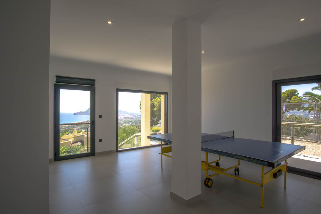 Spielzimmer mit Tischtennisplatte, grauen Fliesenböden und großen Glasfronten mit Panoramablick auf das Mittelmeer und die Bucht von Altea.