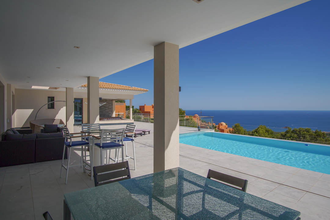 Überdachte Terrasse mit hellem Steinboden, Außen-Essbereich und Infinity-Pool mit Panoramablick auf das Mittelmeer in Altea.