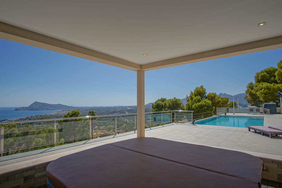 Überdachte Terrasse mit Whirlpool und Panoramablick auf die Bucht von Altea, angrenzend an einen großzügigen Poolbereich mit Glasgeländer.