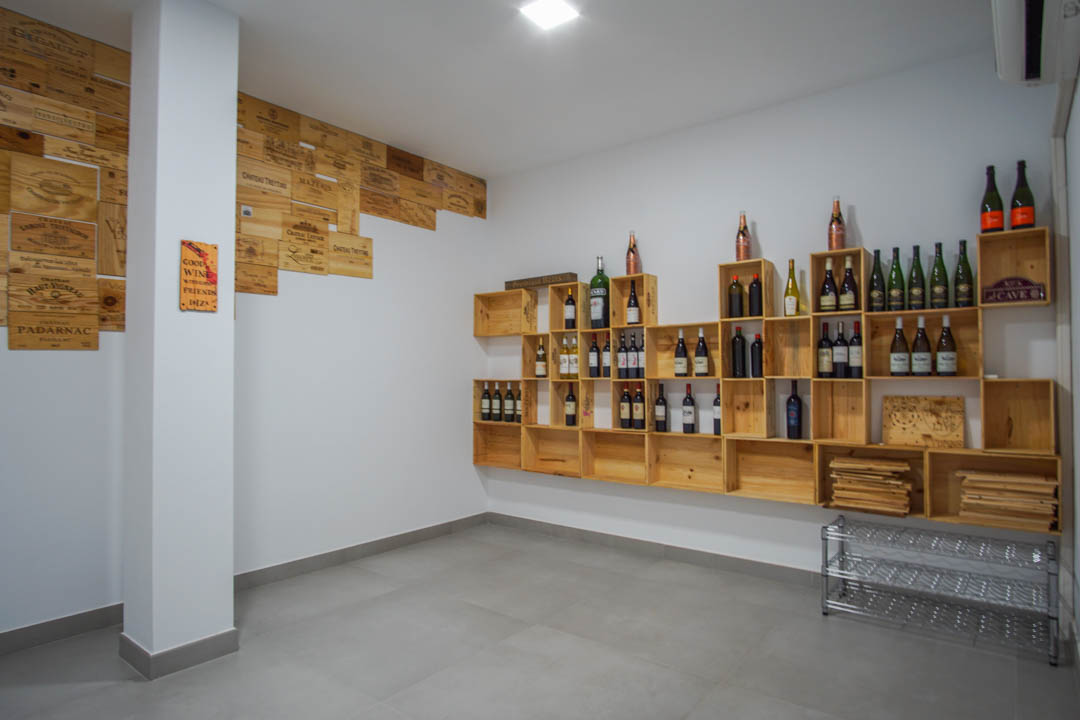 Weinkeller mit modularen Holzregalen aus Weinkisten, dekorativen Wandpaneelen, weißen Wänden und einem modernen grauen Fliesenboden.