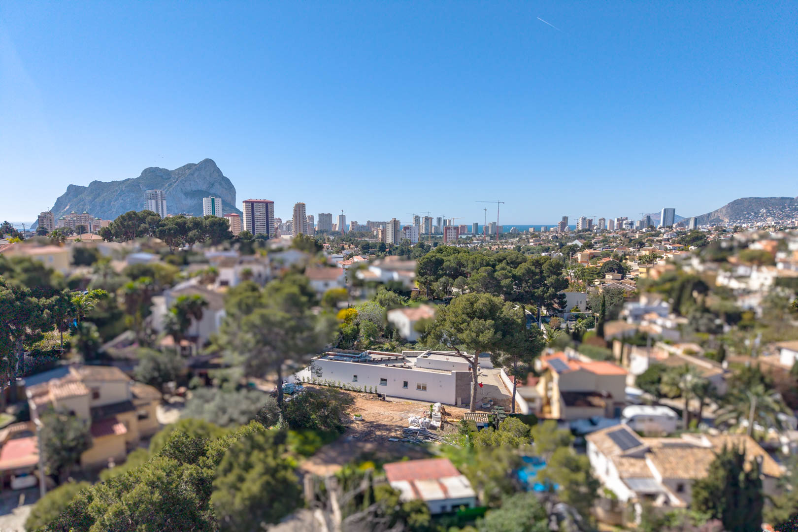 Luftaufnahme der minimalistischen Villa mit dem Peñón de Ifach im Hintergrund. Gezeigt wird der eingeschossige Bau und das Grundstück vor der Außenfertigstellung.
