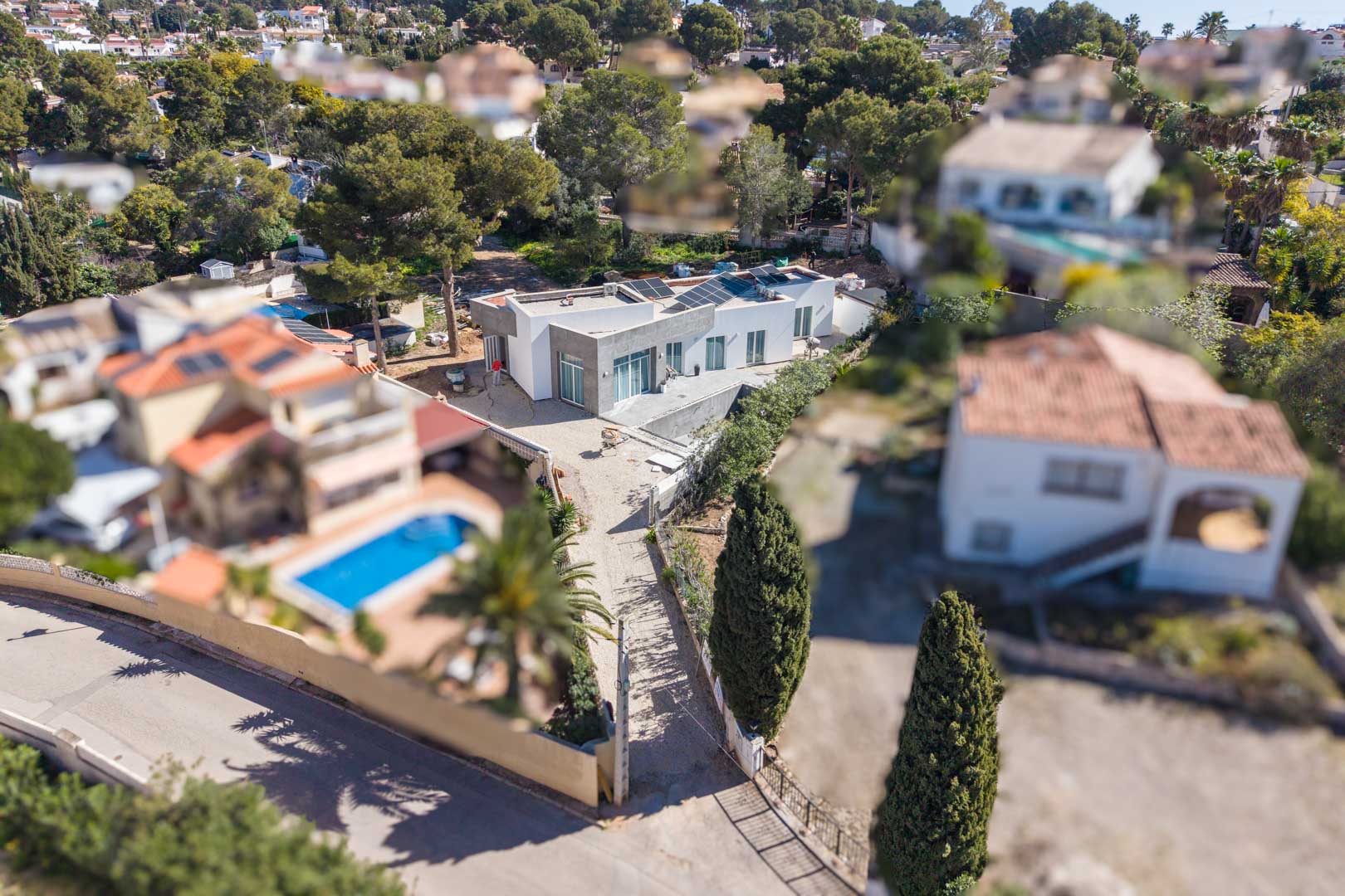 Luftaufnahme der minimalistischen Villa mit Solarmodulen auf dem Flachdach, die das noch fertigzustellende Grundstück in einer etablierten Wohngegend zeigt.
