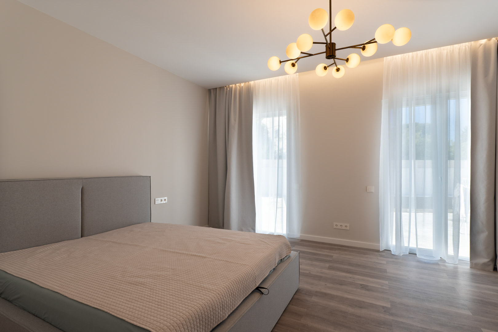 Minimalistisches Hauptschlafzimmer mit grauem Holzboden, indirekter LED-Beleuchtung und einem modernen Molekular-Kronleuchter.