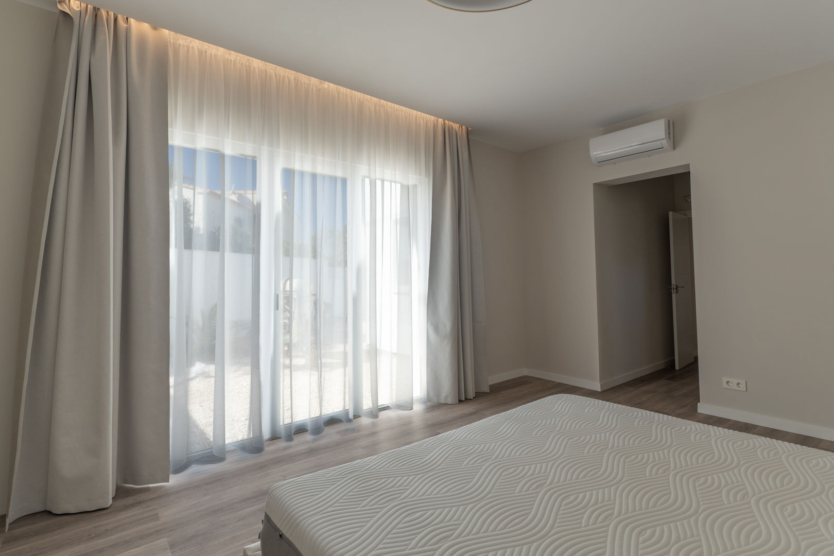Minimalistisches Schlafzimmer mit bodentiefen Glastüren, integrierter LED-Beleuchtung und Klimaanlage. Ausgestattet mit hellem Laminatboden und direktem Zugang zum Außenbereich.