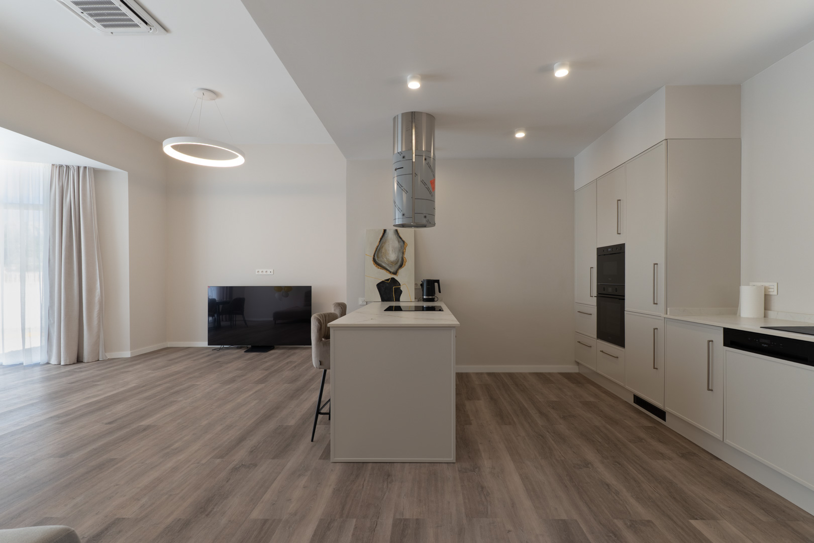 Offene Küche mit zentraler Kochinsel, Arbeitsplatte in Marmoroptik und zylindrischer Dunstabzugshaube, kombiniert mit Laminatboden in Holzoptik.