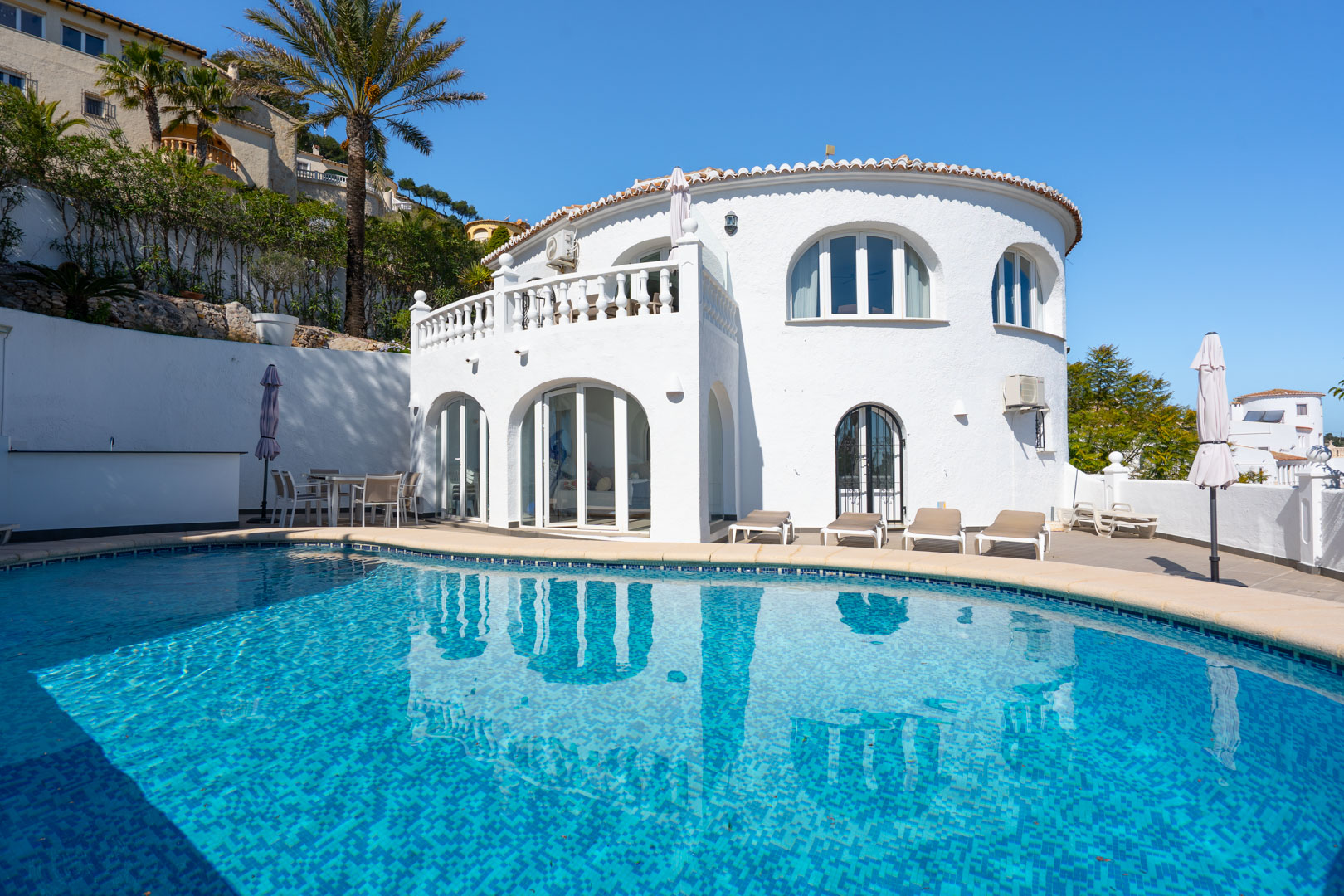 Außenansicht der Villa mit privatem Pool, Sonnenterrasse und verglaster Naya. Die weiße Fassade besticht durch Rundbogenfenster und traditionelle Balustraden.