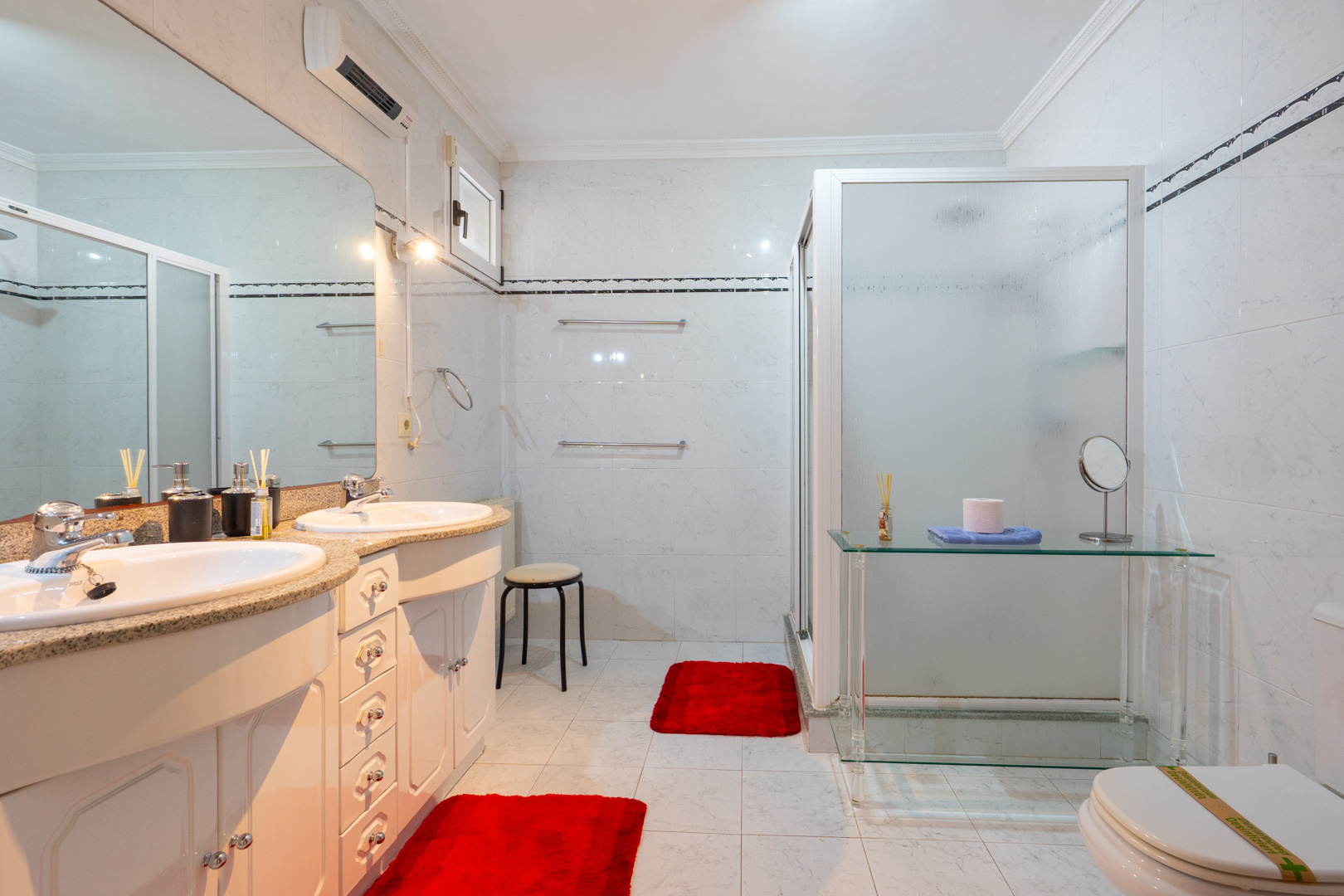 Badezimmer mit Doppelwaschtisch, Granitarbeitsplatte und weißen Schränken. Ausgestattet mit einer Dusche mit Milchglas und einer Klimaanlage.