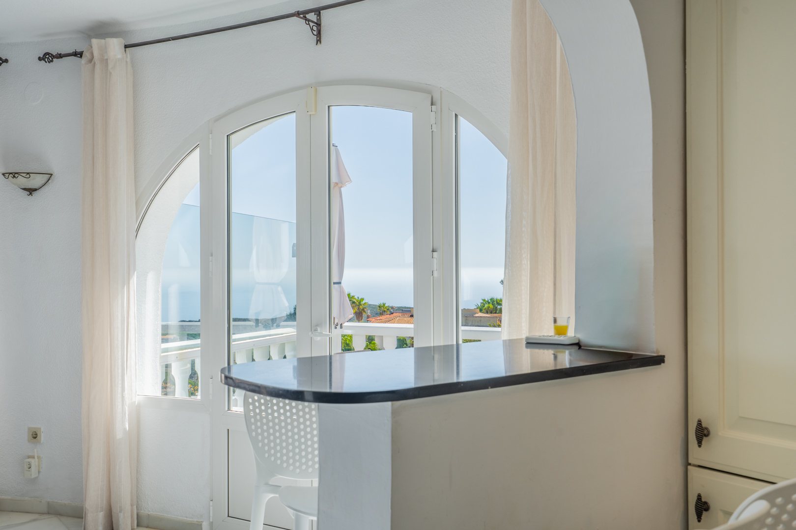 Dunkle Granit-Frühstücksbar unter einem Rundbogen mit Blick auf das Meer durch große bogenförmige Fenstertüren, die zur Terrasse führen.