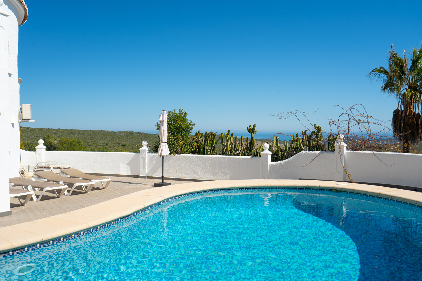 Geschwungener Pool mit angrenzender Sonnenterrasse und Liegestühlen, die einen weiten Blick auf das Mittelmeer und die umliegende Hügellandschaft bietet.