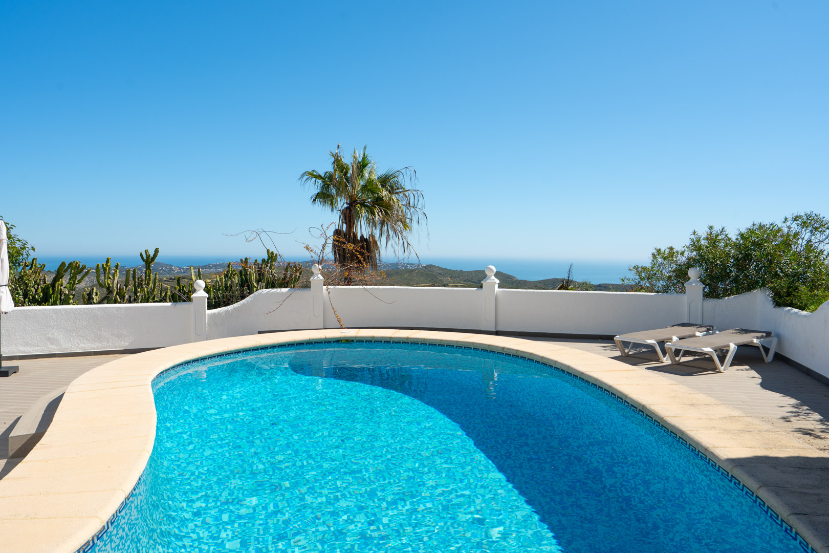 Geschwungener Pool mit Panoramablick auf das Mittelmeer, umgeben von einer Sonnenterrasse mit Liegestühlen und traditionellen weißen Mauern.