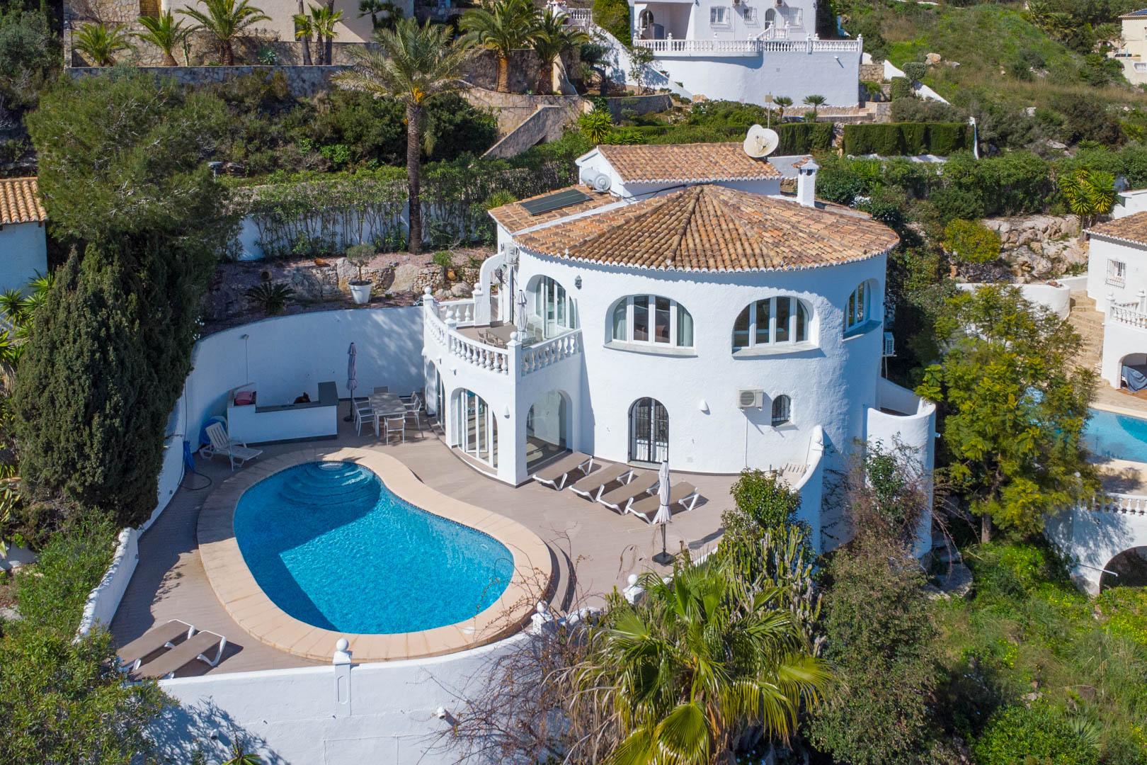 Luftaufnahme der Villa mit nierenförmigem Pool, großzügiger Sonnenterrasse, traditioneller weißer Fassade und Sonnenkollektoren auf dem Ziegeldach.