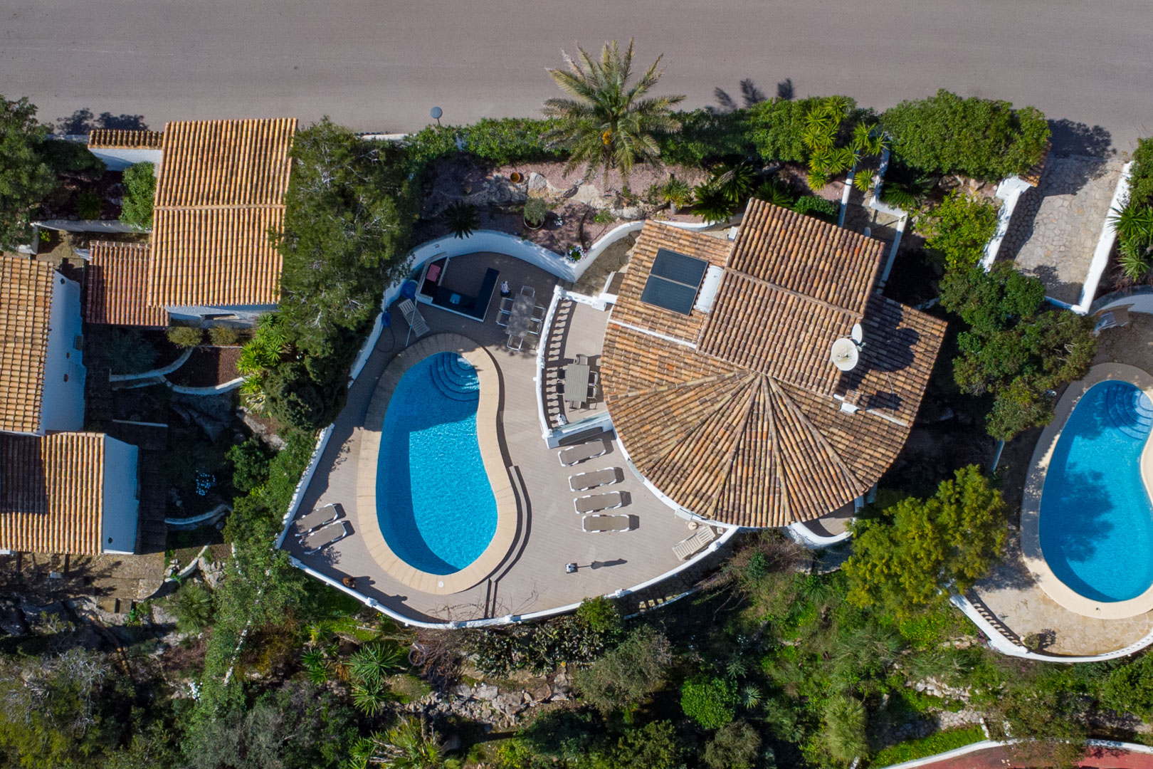 Luftbild der Immobilie mit nierenförmigem Pool, großzügiger Sonnenterrasse mit Essbereich und traditionellem Ziegeldach mit Photovoltaikanlage.