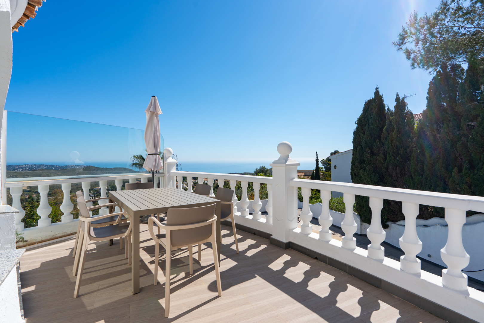 Obere Terrasse mit weißer Balustrade, modernen Essmöbeln und Panoramablick auf das Mittelmeer und den angrenzenden Naturpark.