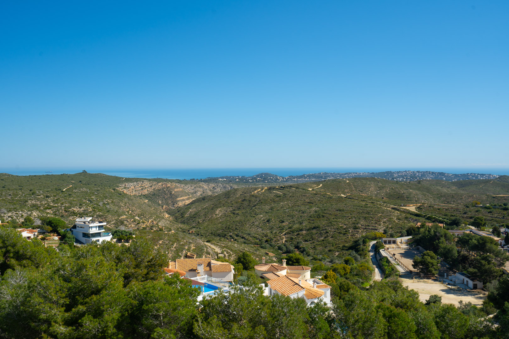 Panoramablick vom Anwesen auf den Naturpark Granadella und das Mittelmeer, mit sanften grünen Hügeln und der fernen Küstenlinie unter blauem Himmel.