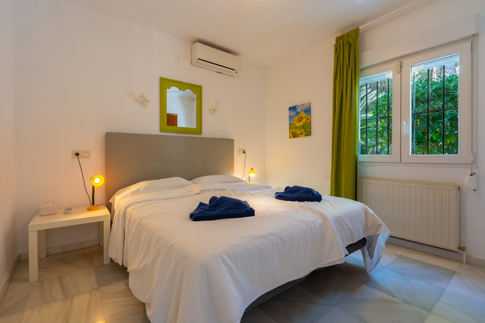 Schlafzimmer mit Marmorboden, Klimaanlage und Heizung. Es verfügt über ein Fenster mit Sicherheitsgittern, grüne Vorhänge und einen passenden Zierspiegel.