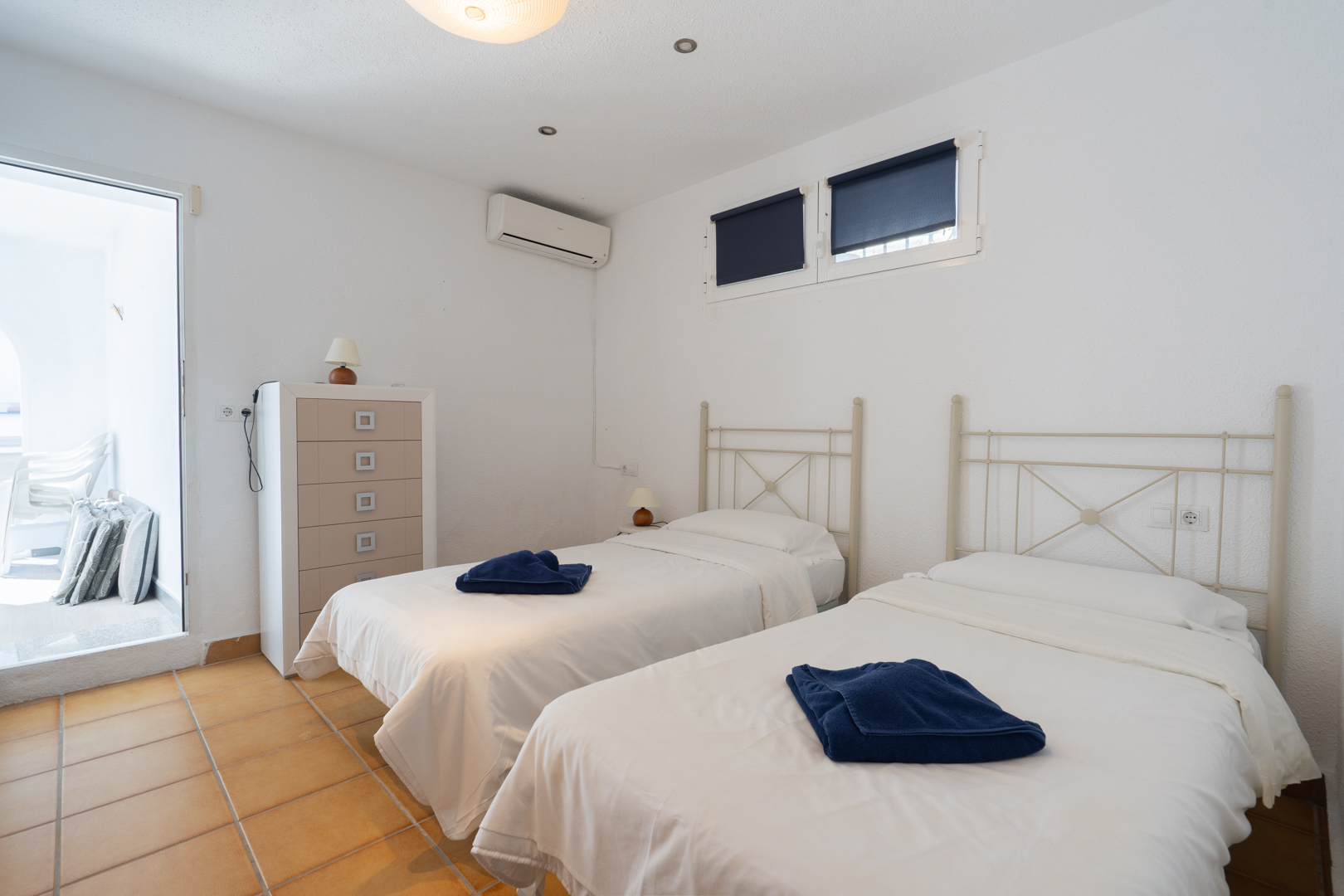 Schlafzimmer mit zwei Einzelbetten, Terrakotta-Fliesenboden und Klimaanlage. Mit direktem Zugang zur Terrasse und viel natürlichem Licht.