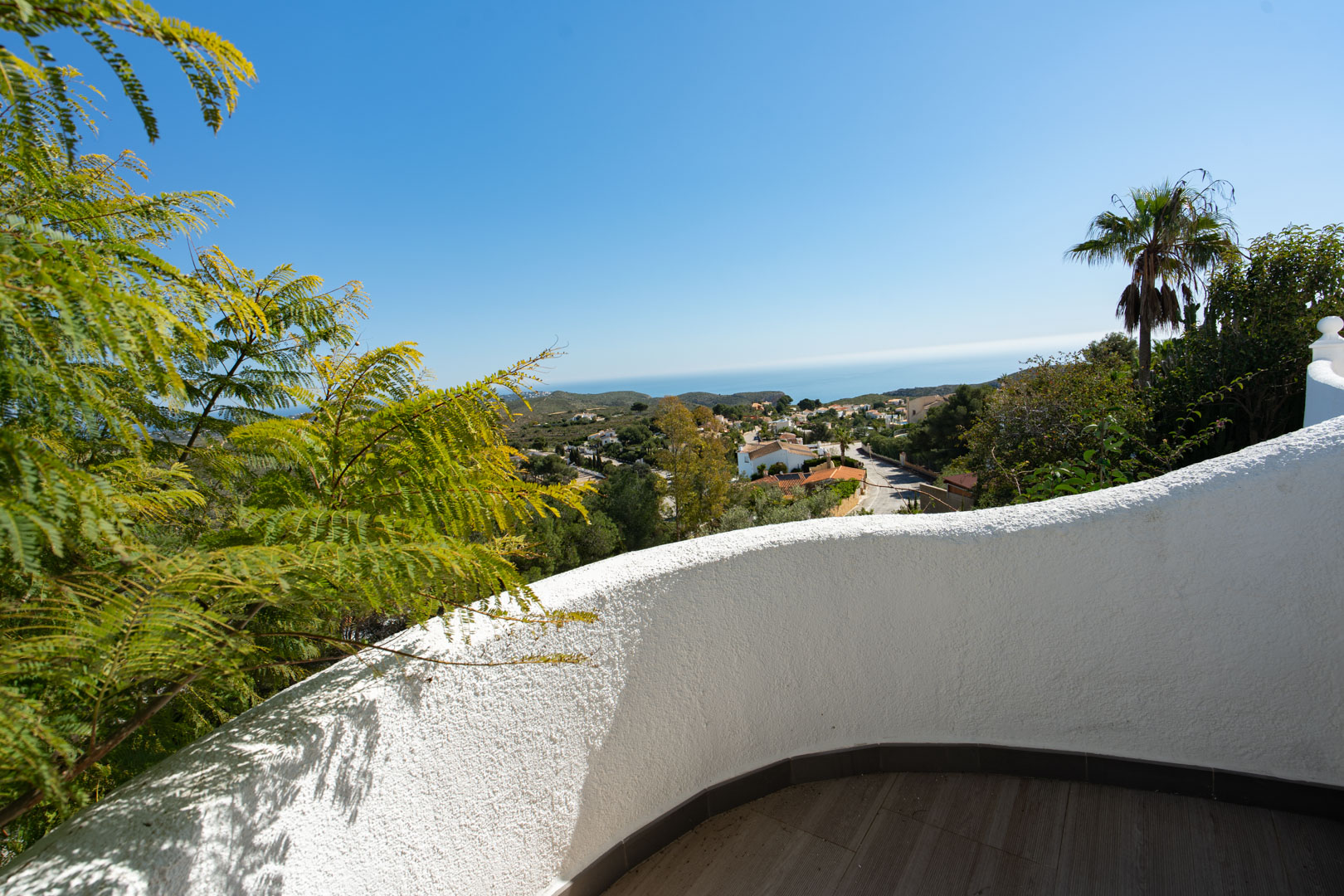 Terrasse mit geschwungener, weißer Putzwand und dunklem Fliesenboden, die einen weiten Blick auf das Mittelmeer und die Siedlung Cumbre del Sol bietet.