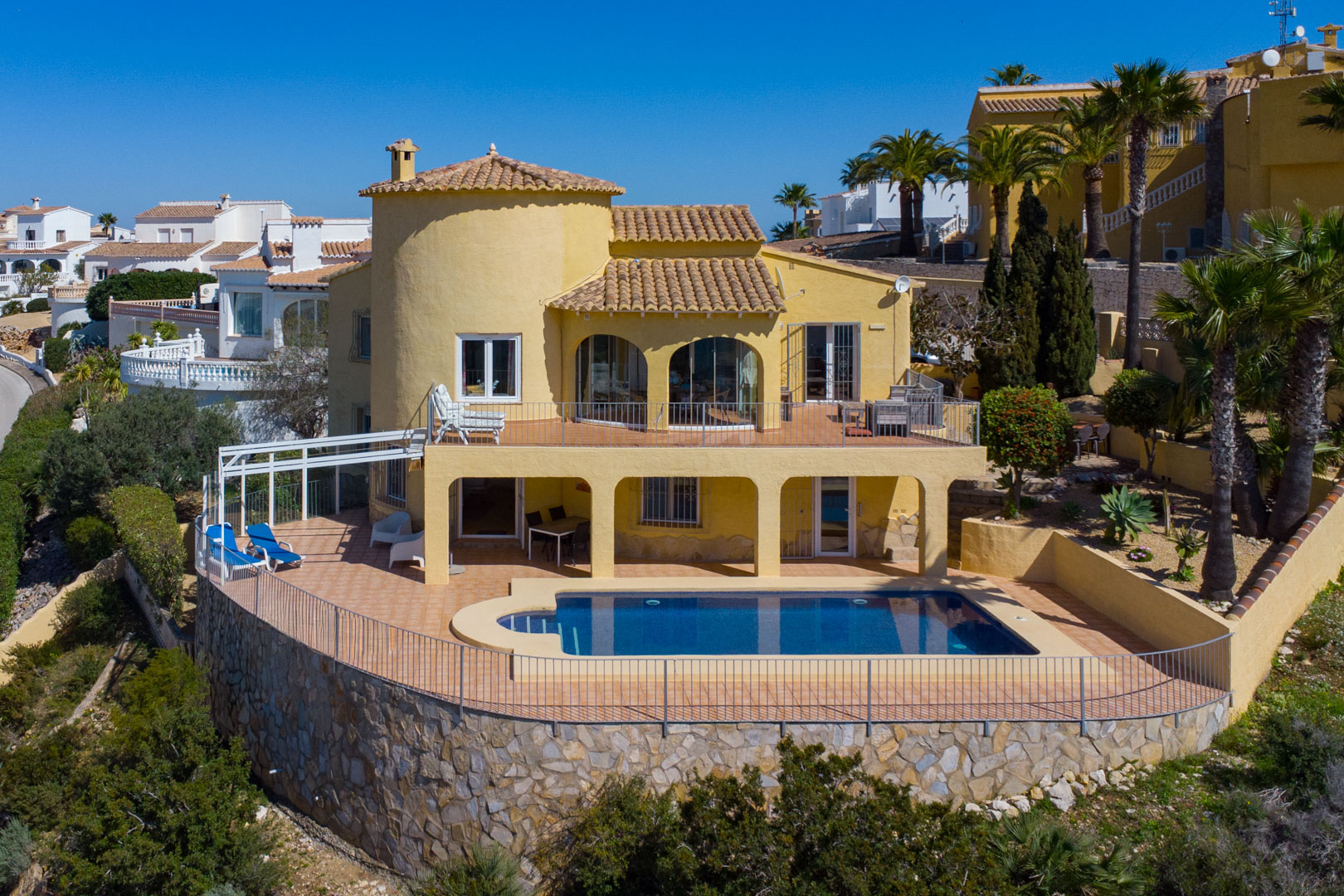Außenansicht der Villa mit privatem Pool, weitläufigen Terracotta-Terrassen auf zwei Ebenen und einer markanten Stützmauer aus Natursteinmauerwerk.
