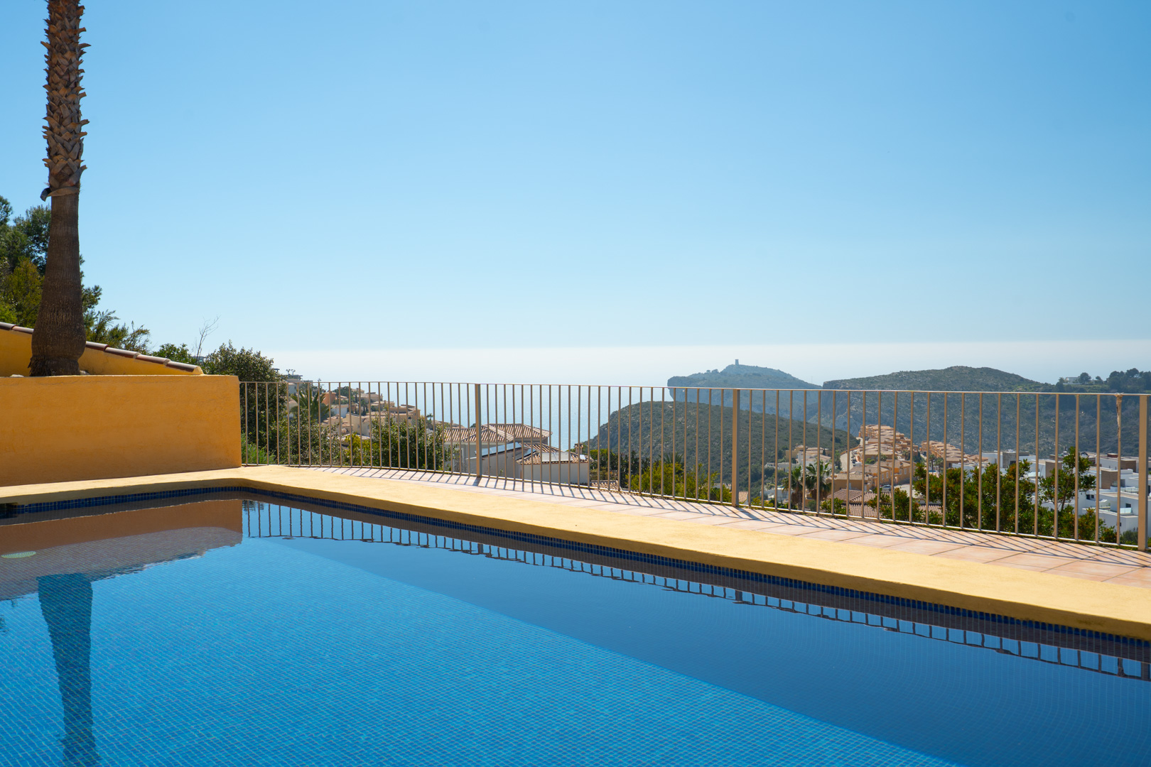 Blau gefliester Pool mit Panoramablick auf das Meer und das Cap d’Or in Moraira, umgeben von einer Terrasse mit schlichtem Metallgeländer.