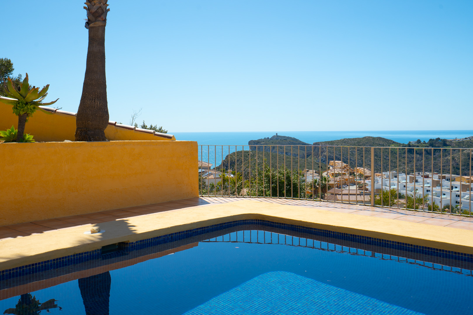 Blau gefliester Pool und Sonnenterrasse mit Panoramablick auf das Mittelmeer und das Cap d'Or in Moraira, eingefasst von einem schlichten Metallgeländer.
