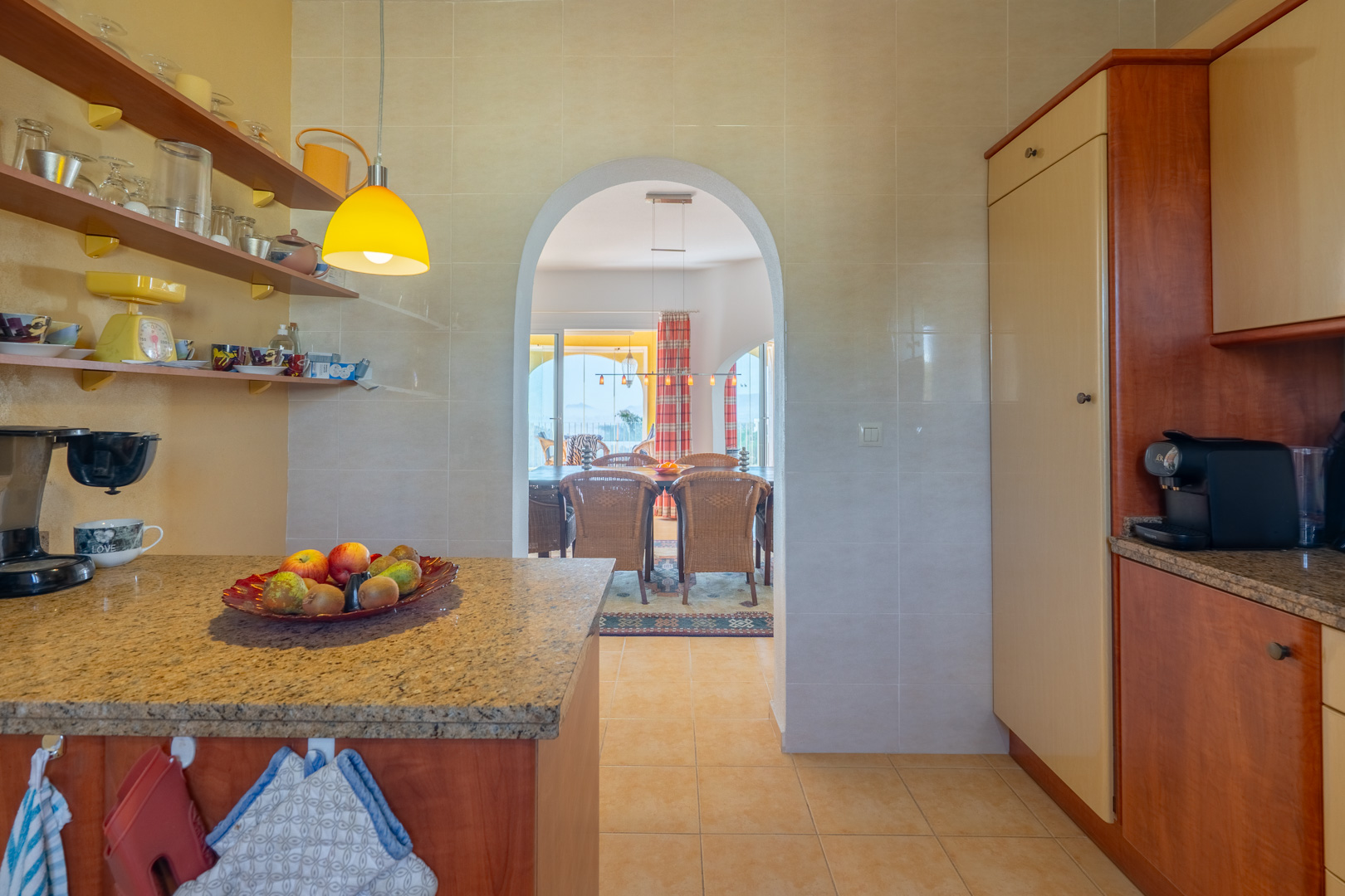 Funktionale Küche mit Granitarbeitsplatten und offenem Regal, verbunden durch einen Rundbogen mit dem Esszimmer und der Terrasse.