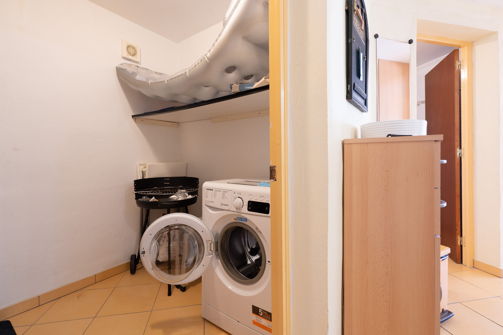 Funktionaler Hauswirtschaftsraum mit Frontlader-Waschmaschine, praktischer Ablagefläche und hellen Bodenfliesen.