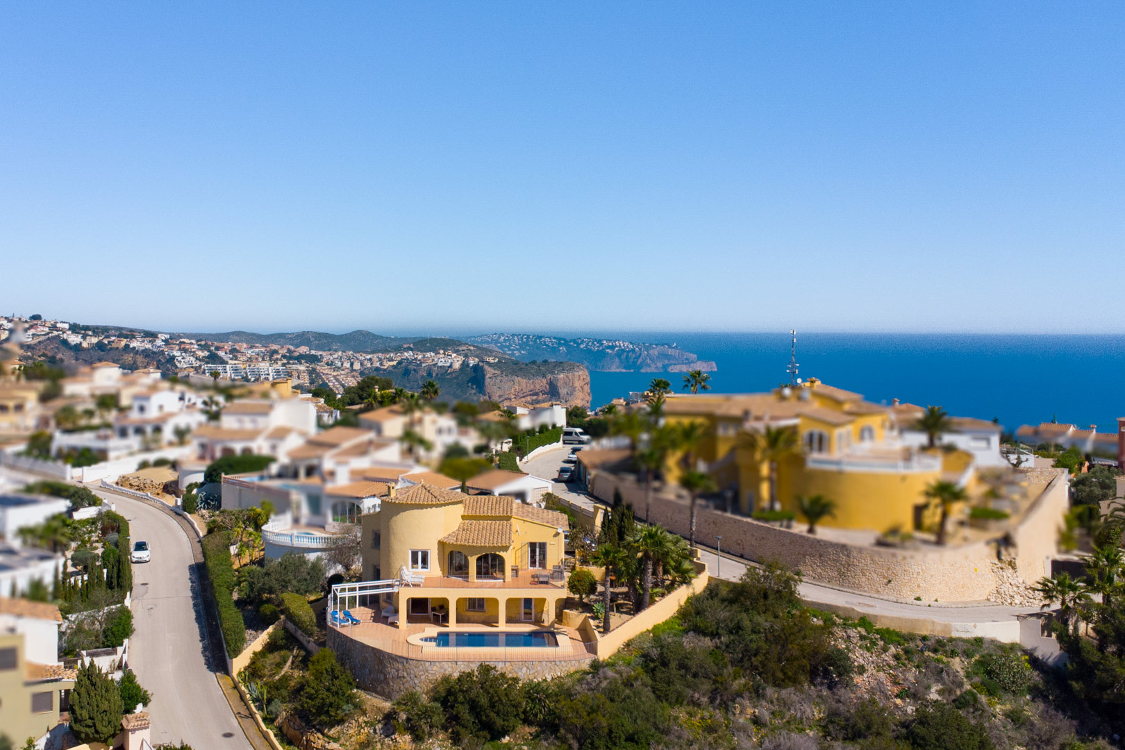 Luftaufnahme der gelben Villa mit privatem Pool und mehreren Terrassen, die einen Panoramablick auf das Mittelmeer und das Cap d’Or in Moraira bieten.