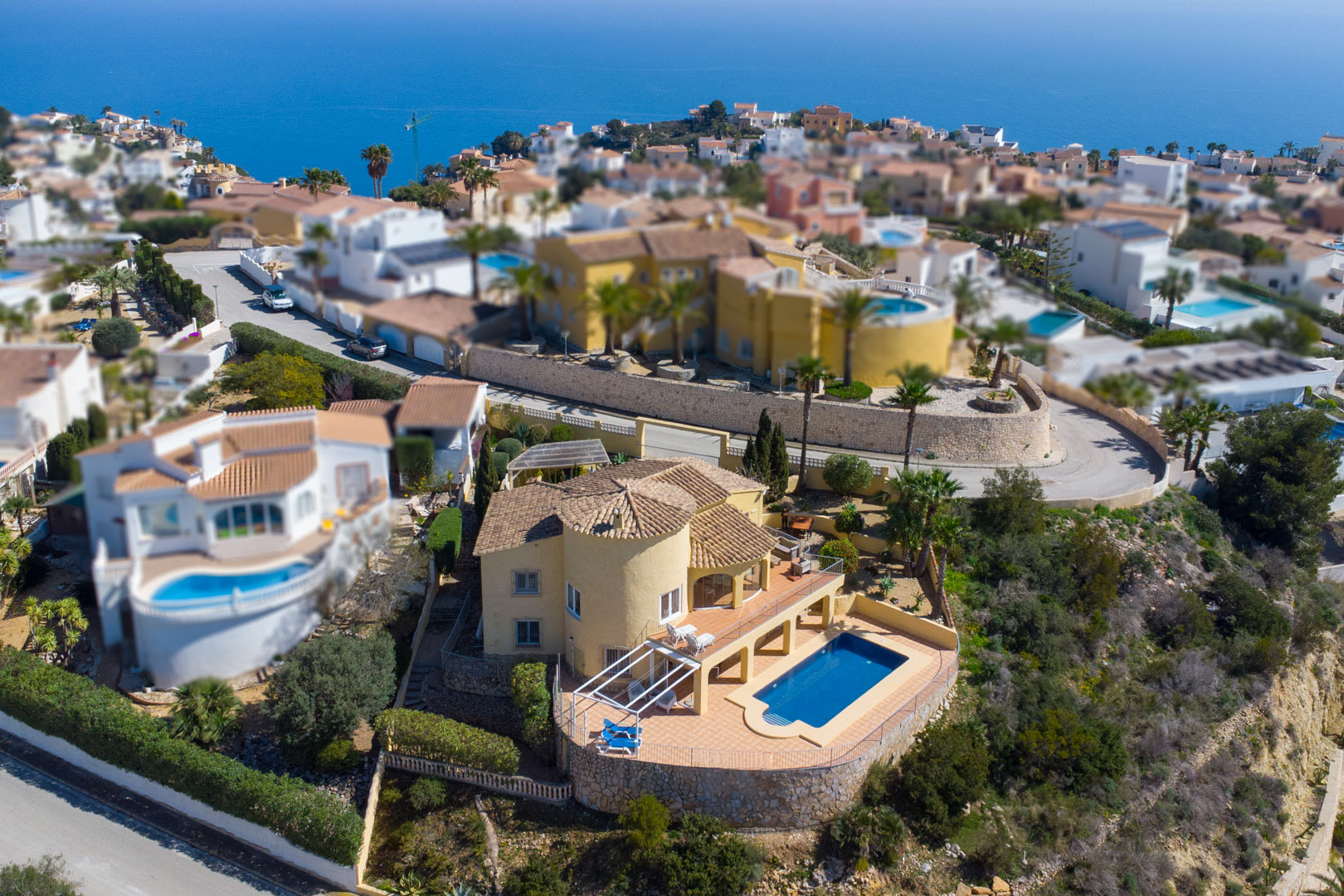 Luftaufnahme der traditionellen Villa mit gelber Fassade, Rundturm und privatem Poolbereich, umgeben von einer weitläufigen Terrasse mit Meerblick.