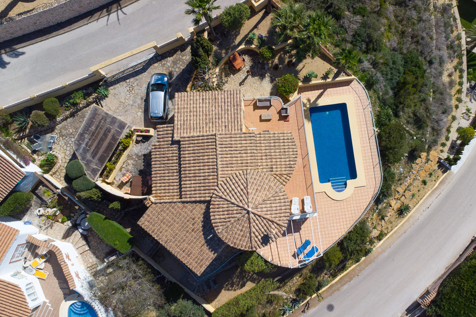 Luftbild der Villa mit Darstellung der traditionellen Dachstruktur, des rechteckigen Pools auf der Terrasse und der privaten Einfahrt mit Carport-Stellplatz.