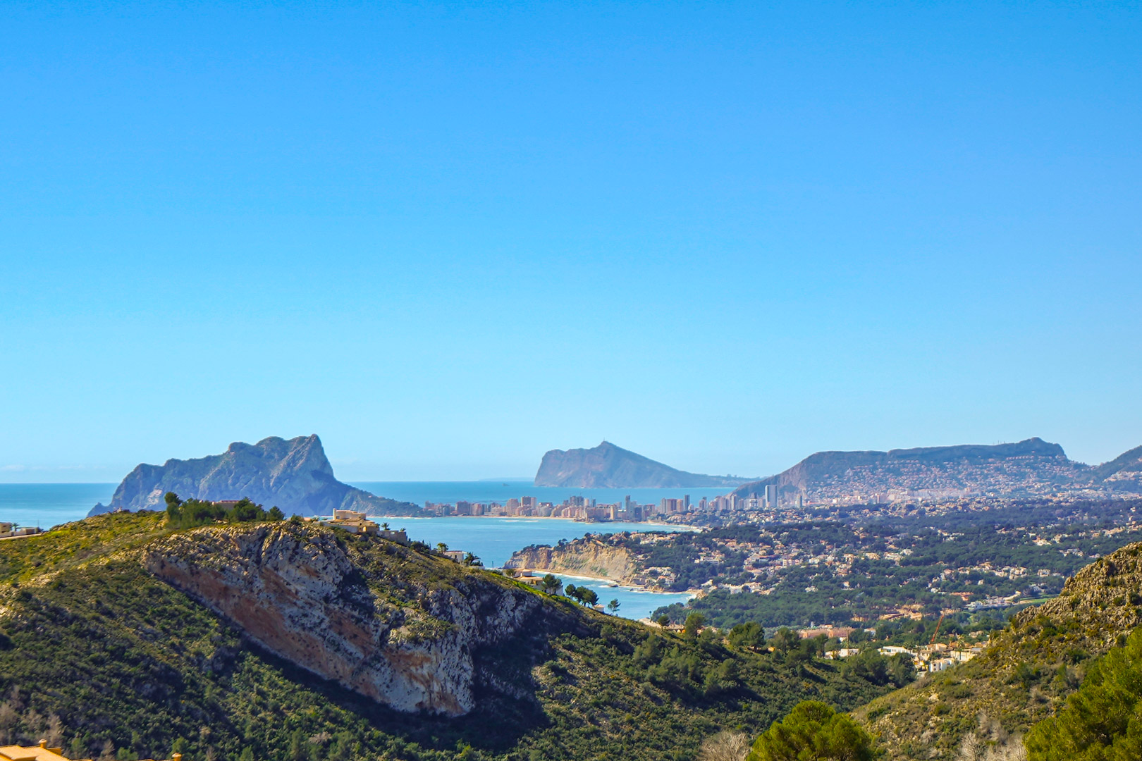 Panoramablick von der Immobilie auf den Peñón de Ifach in Calpe, die Küste von Benissa und die Skyline von Benidorm am Horizont unter blauem Himmel.