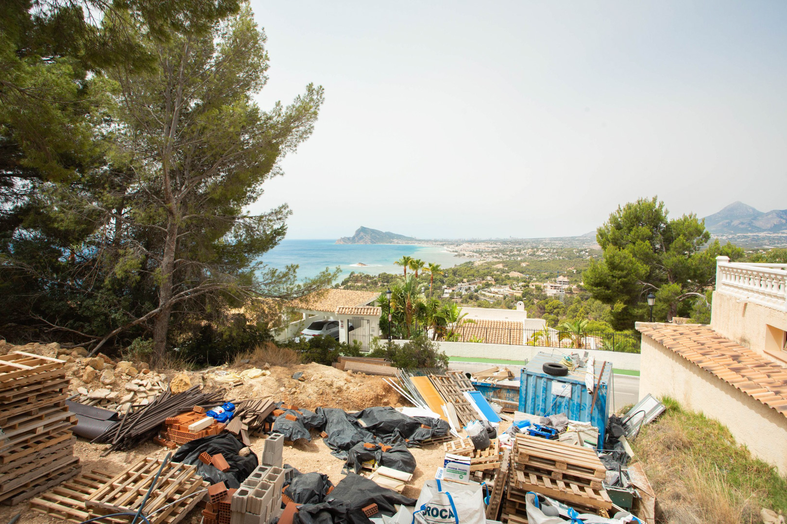 Erhöhter Blick vom Grundstück in Altea Hills mit Baumaterialien und einem freien Panorama auf das Mittelmeer und die Küste von Altea.
