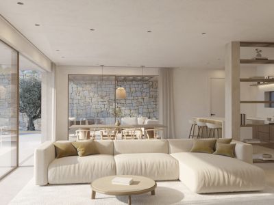 Geräumiger Wohnbereich mit hellem Ecksofa und rundem Couchtisch. Große Glastüren führen zu einer Außenterrasse mit Natursteinmauer und altem Olivenbaum.