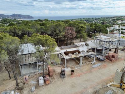 Luftaufnahme der im Bau befindlichen Villa, die ihre Betonstruktur und Baumaterialien zeigt. Im Hintergrund sind das Mittelmeer und die bewaldete Landschaft zu sehen.