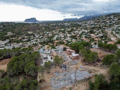 Luftaufnahme von Villen im Bau in einem Wohngebiet von Moraira, mit Kränen und Fundamenten, umrahmt vom Meer und dem Peñón de Ifach in der Ferne.