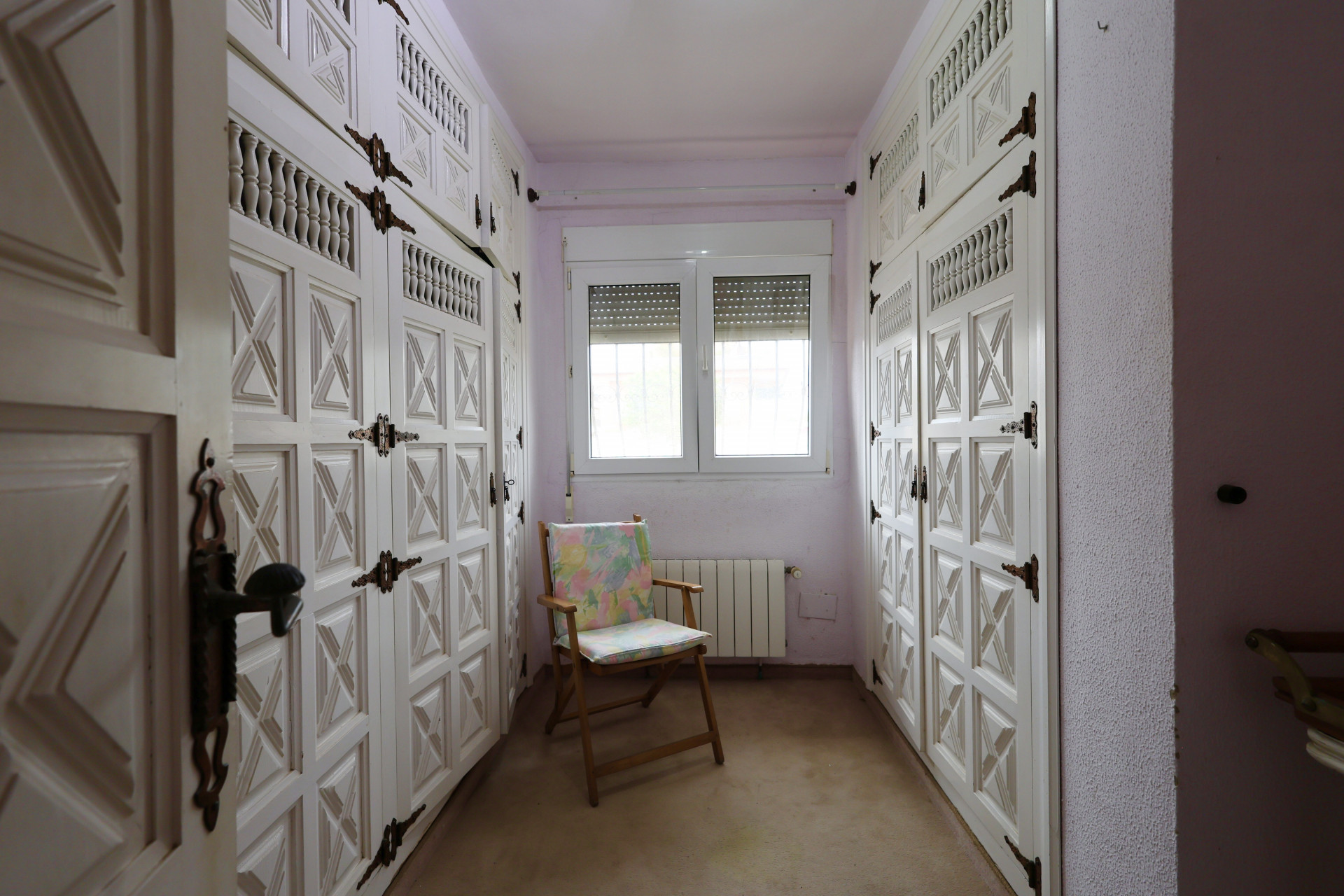 Ankleidezimmer mit weißen Einbauschränken und Eisenbeschlägen, beleuchtet durch ein Fenster.