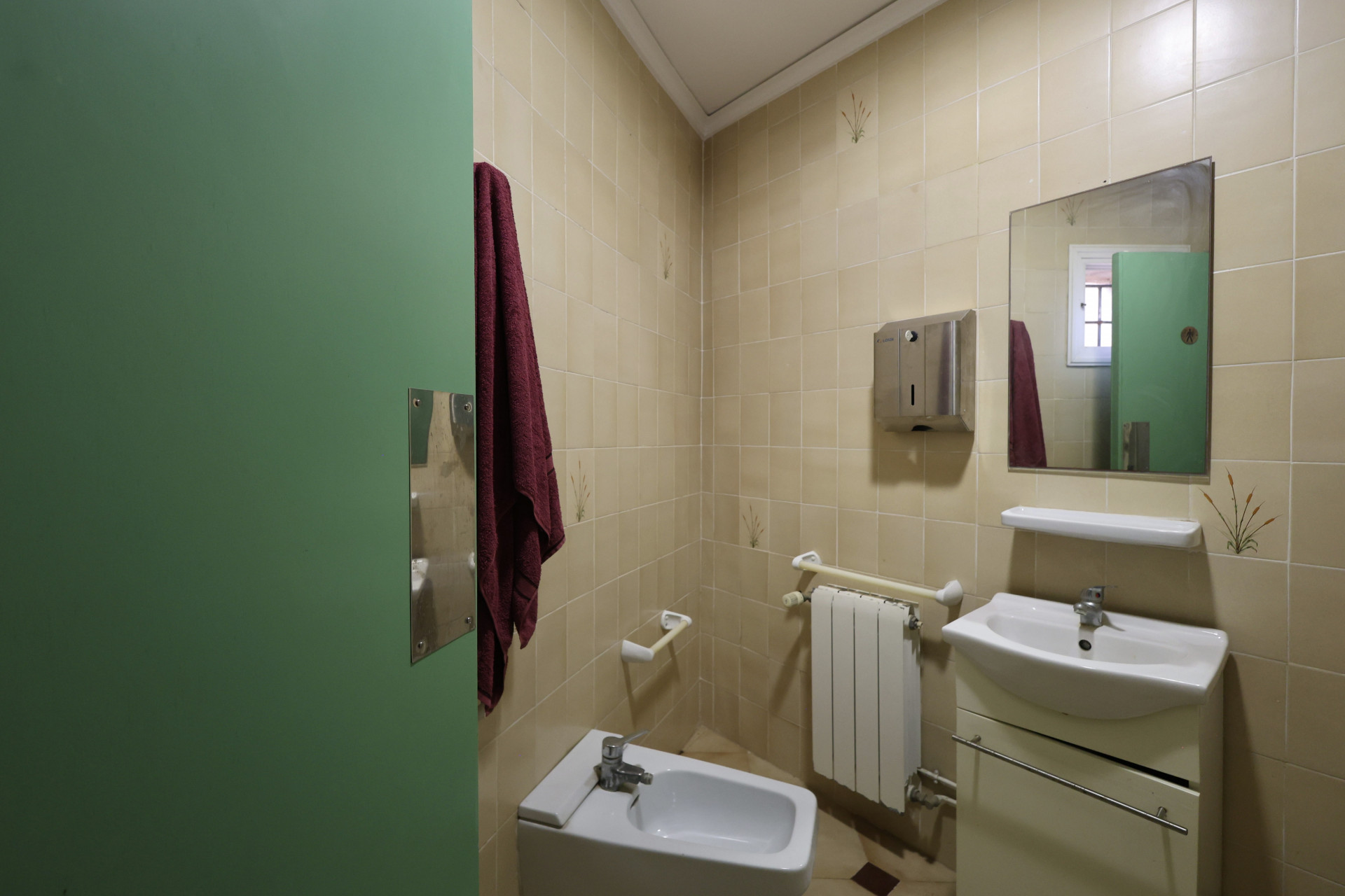 Badezimmer mit cremefarbenen Fliesen, weißem Bidet und grüner Tür.