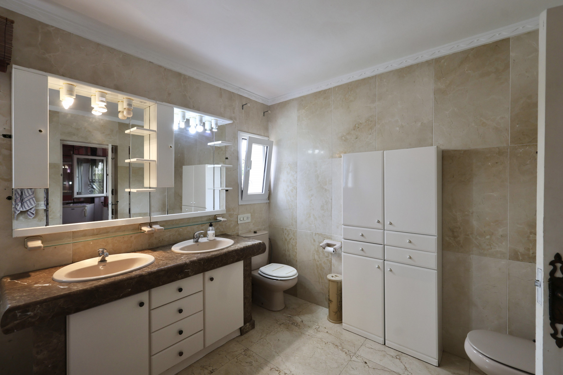 Badezimmer mit Doppelwaschbecken, Marmorplatte und weißen Schränken.