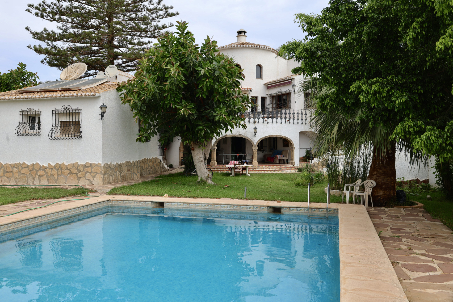 Blick auf den türkisfarbenen Pool und die weiße Fassade der Villa mit Steindetails und Garten.