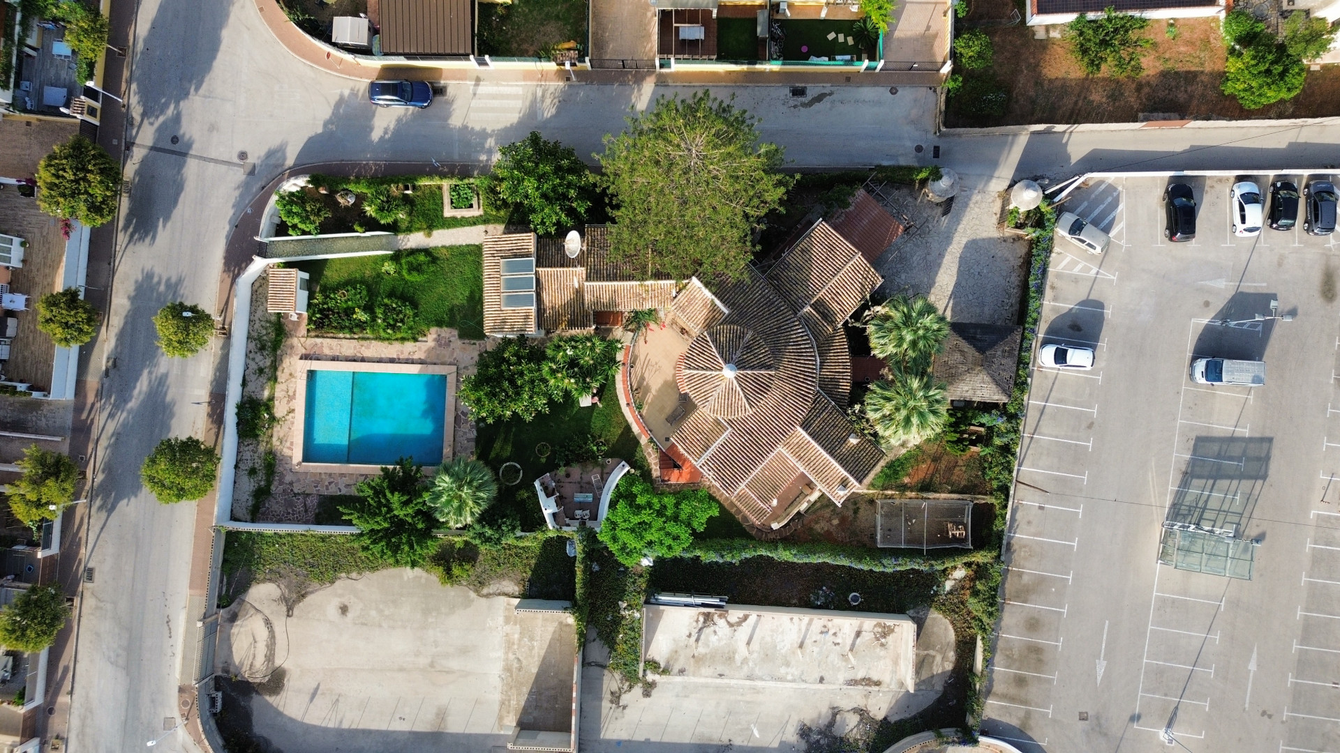 Luftaufnahme der Villa mit Pool und Ziegeldach, umgeben von Grün und angrenzendem Parkplatz.