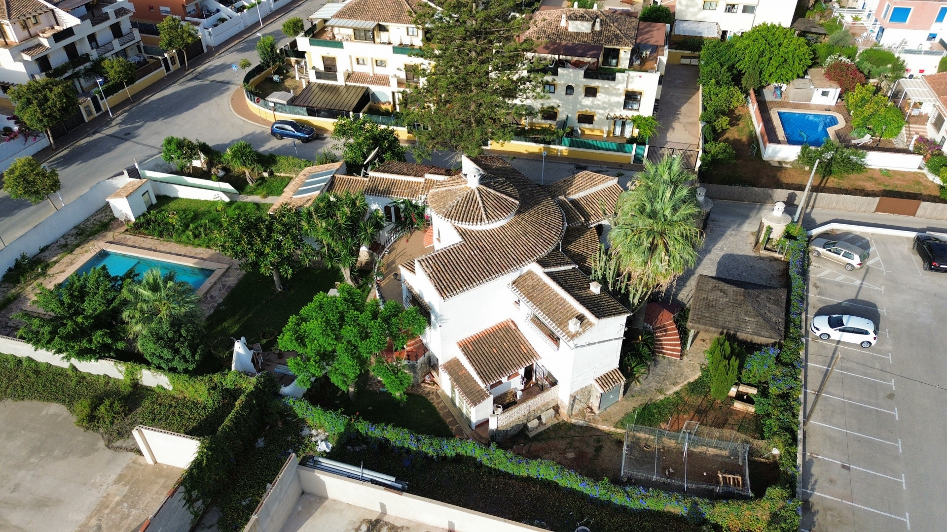 Luftaufnahme der Villa mit Ziegeldach, Pool umgeben von Grün und angrenzendem Parkplatz.