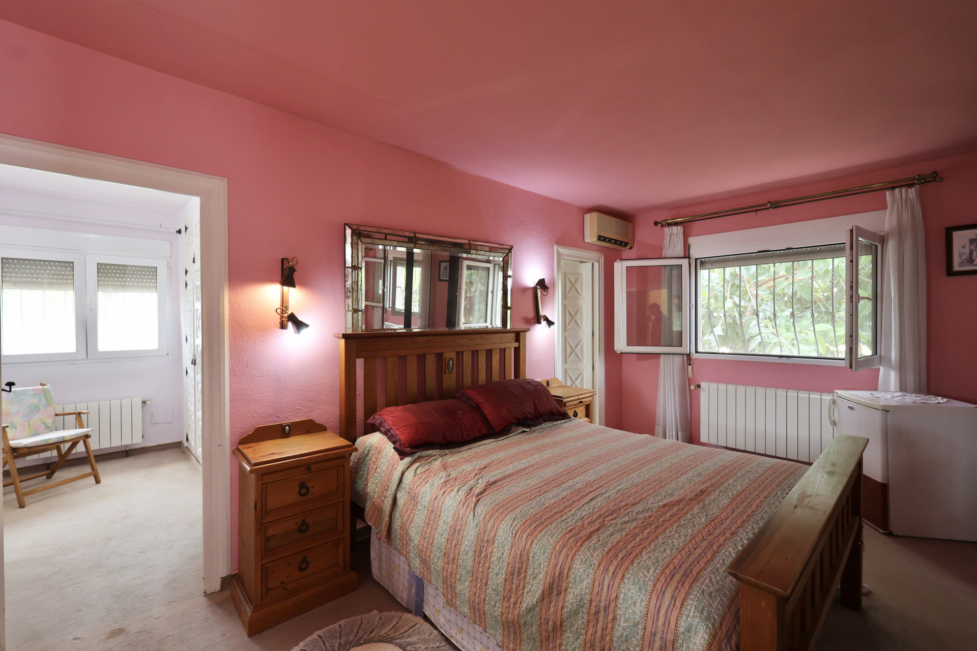 Schlafzimmer mit rosa Wänden, Holzbett und Spiegel mit Wandleuchten. Renovierungsbedürftig.