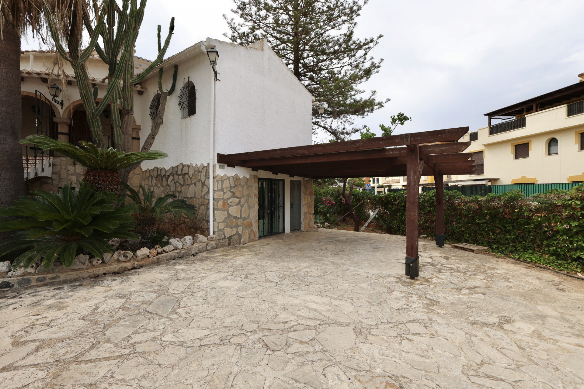 Villaeingang mit unregelmäßigem Steinboden und überdachter Garage mit Holzkonstruktion.