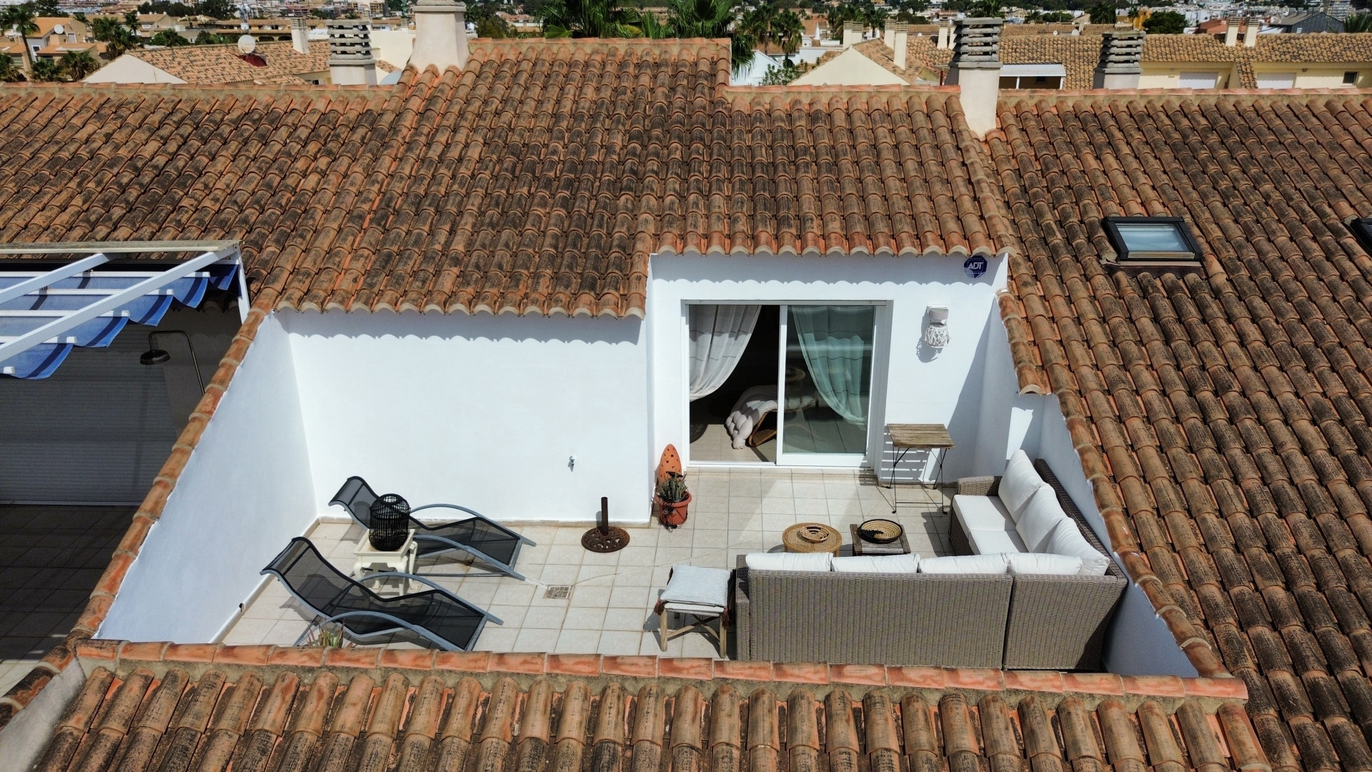 Erhöhte Ansicht der sonnendurchfluteten Terrasse mit Gartenmöbeln und Zugang zum Innenraum.