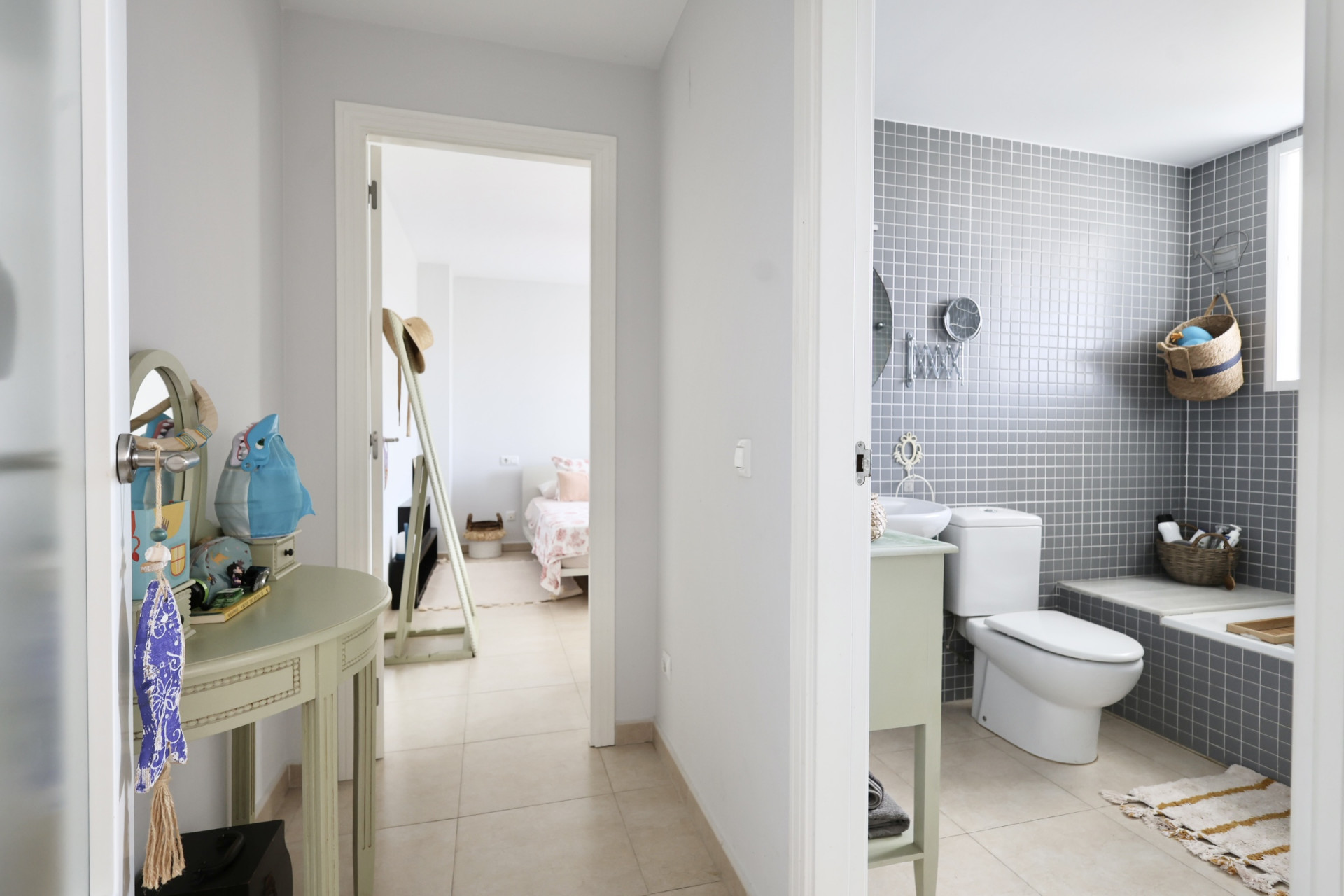 Flurdetail mit dekorativer Konsole und Blick ins Badezimmer mit grauen Fliesen und Schlafzimmer im Hintergrund.