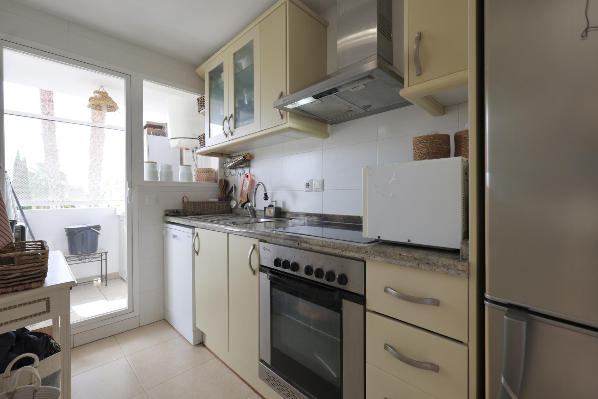 Helle Küche mit Granit-Arbeitsplatten, Edelstahlgeräten und Zugang zum Balkon.