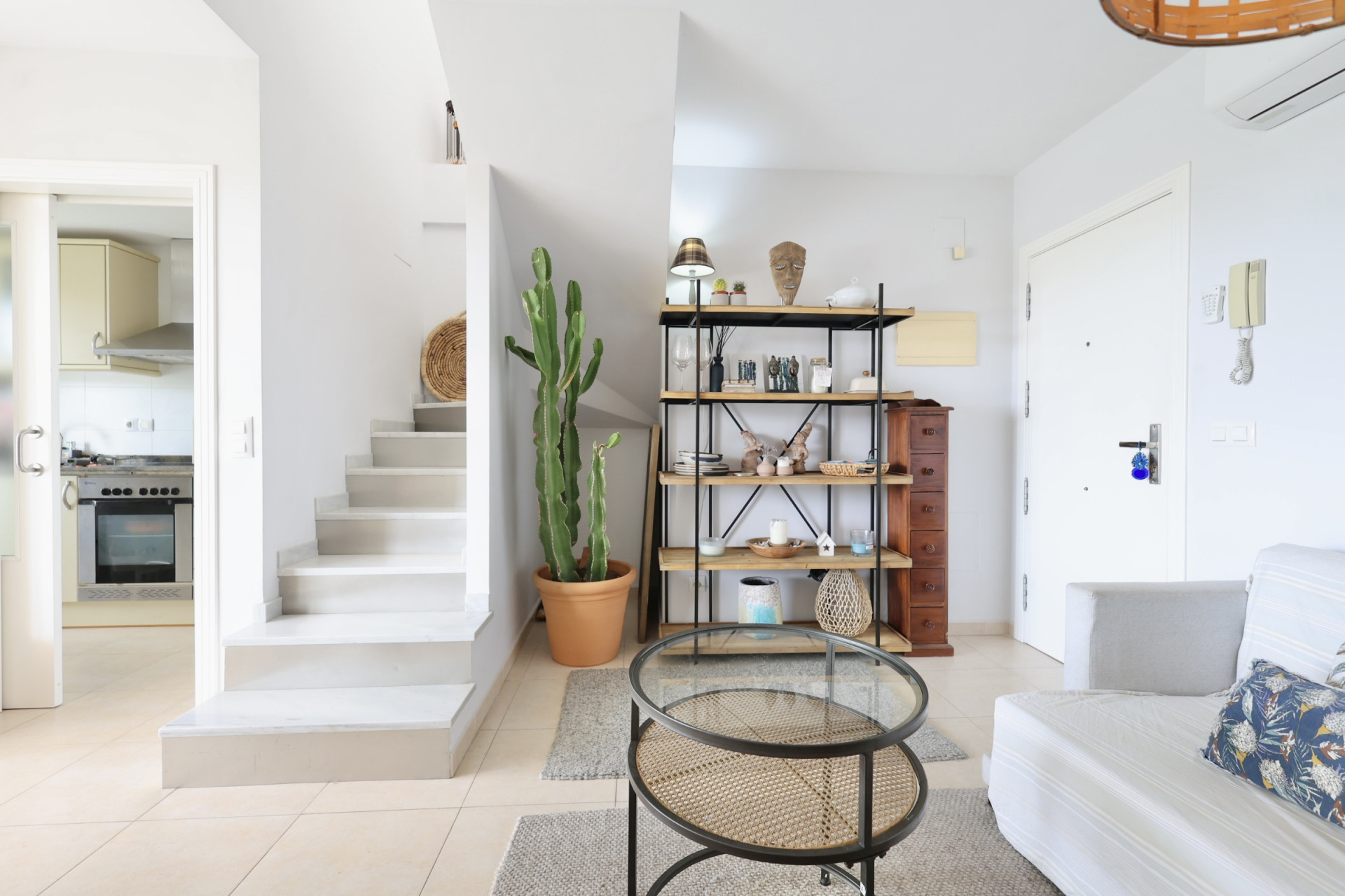 Helles Interieur mit weißer Treppe, Holz- und Metallregal und Couchtisch aus Rattan.