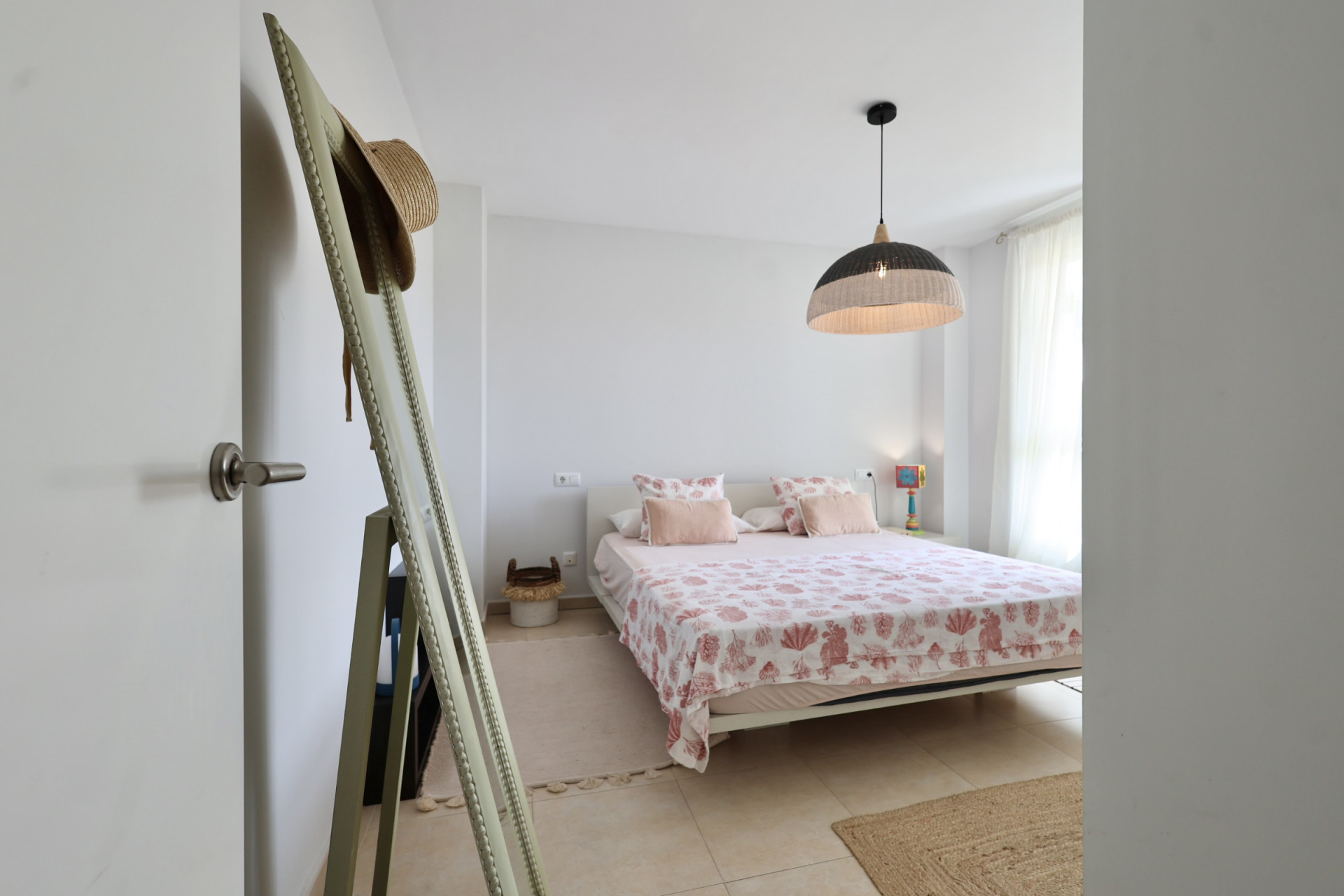 Helles Schlafzimmer mit Doppelbett, Bettwäsche mit Meeresmotiven und einer Hängelampe aus Korbgeflecht.