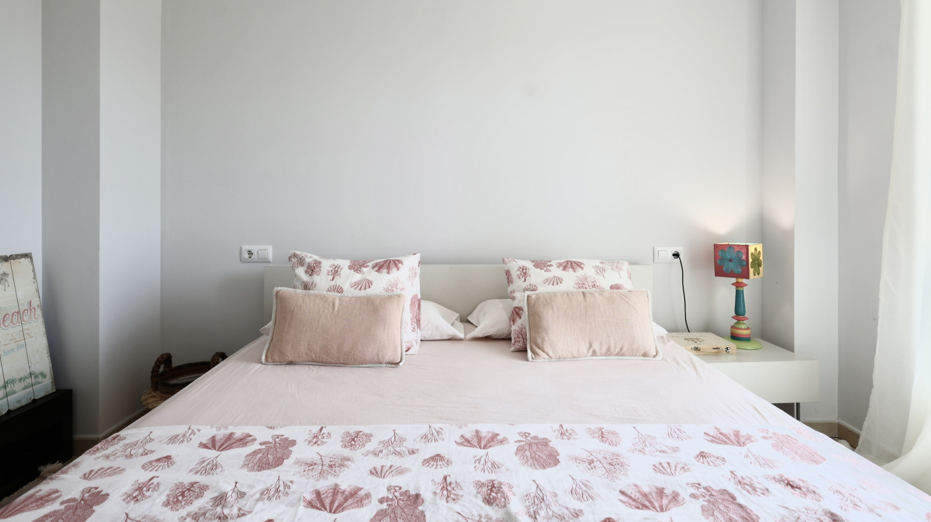 Helles Schlafzimmer mit Doppelbett, Bettwäsche mit Meeresmotiven und weißem Nachttisch mit dekorativer Lampe.